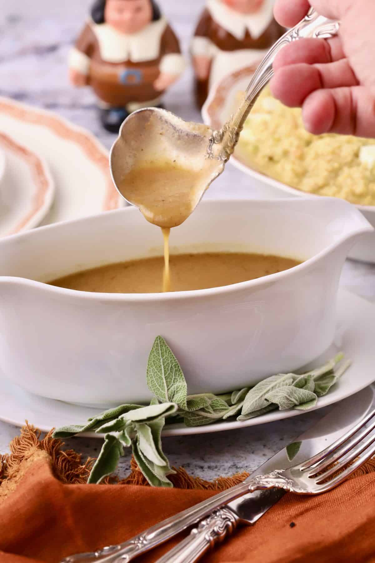 Turkey neck gravy in a white gravy boat with gravy falling from a gravy ladle.