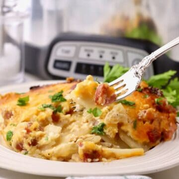 A serving of ham and scalloped potatoes with a crock pot in the back ground.