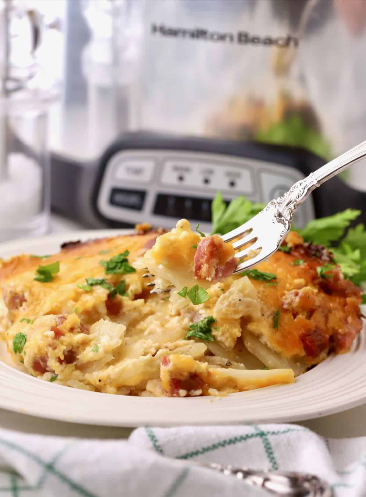 A serving of ham and scalloped potatoes cooked in a crock pot on a white plate with a fork. 