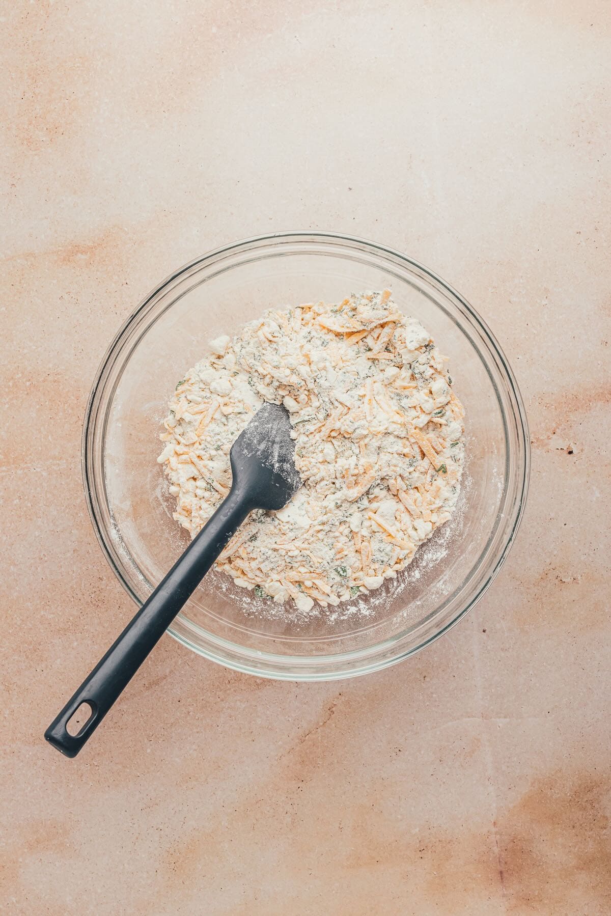 Shredded cheese and chopped herbs in a bowl of flour and other dry ingredients. 