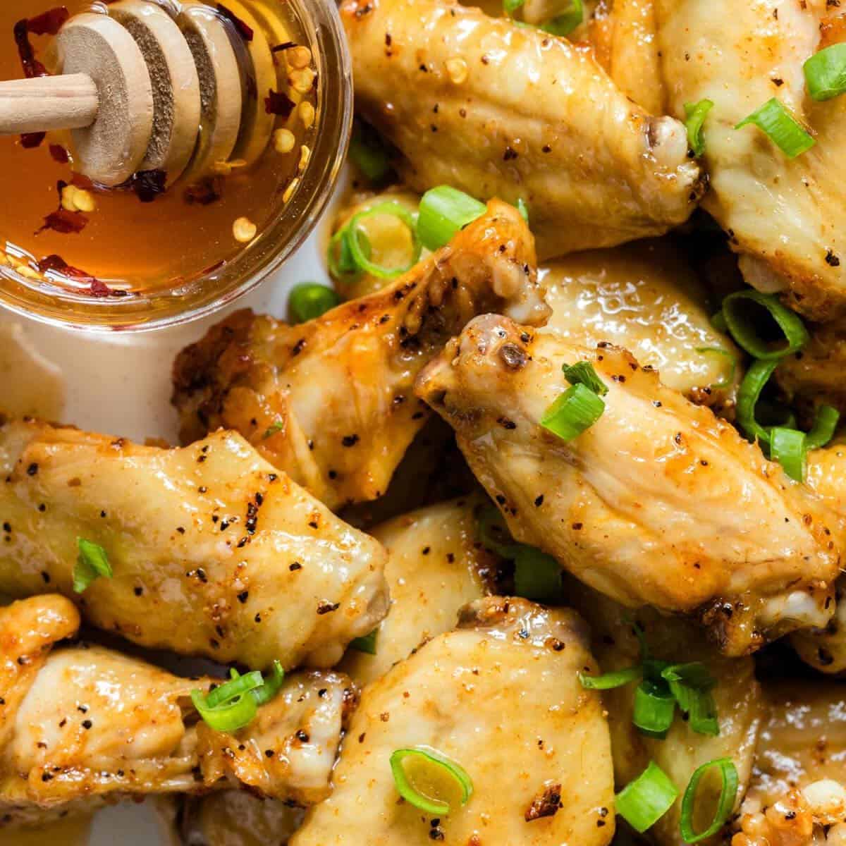 Hot honey chicken wings on a plate with a cup of hot honey and a wooden honey dipper.