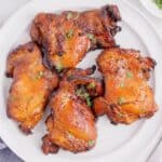 Four boneless, skinless chicken thighs cooked in an air fryer on a white plate.