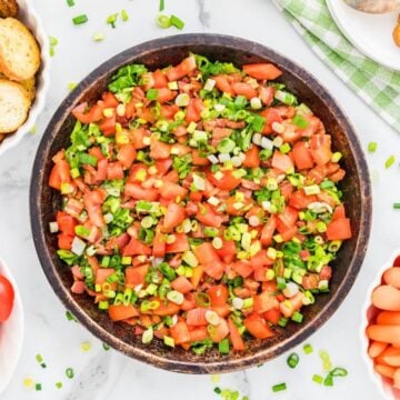A wooden bowl full of BLT Dip topped with bacon, lettuce, and tomatoes.