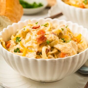 A white bowl full of crack chicken noodle soup garnished with bits of bacon and parsley.