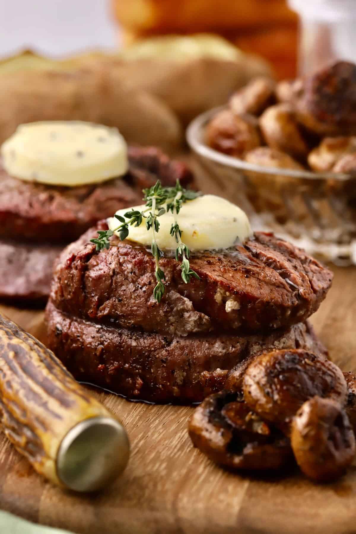 Two filet mignon steaks topped with a pat of garlic herb butter and thyme sprigs. 