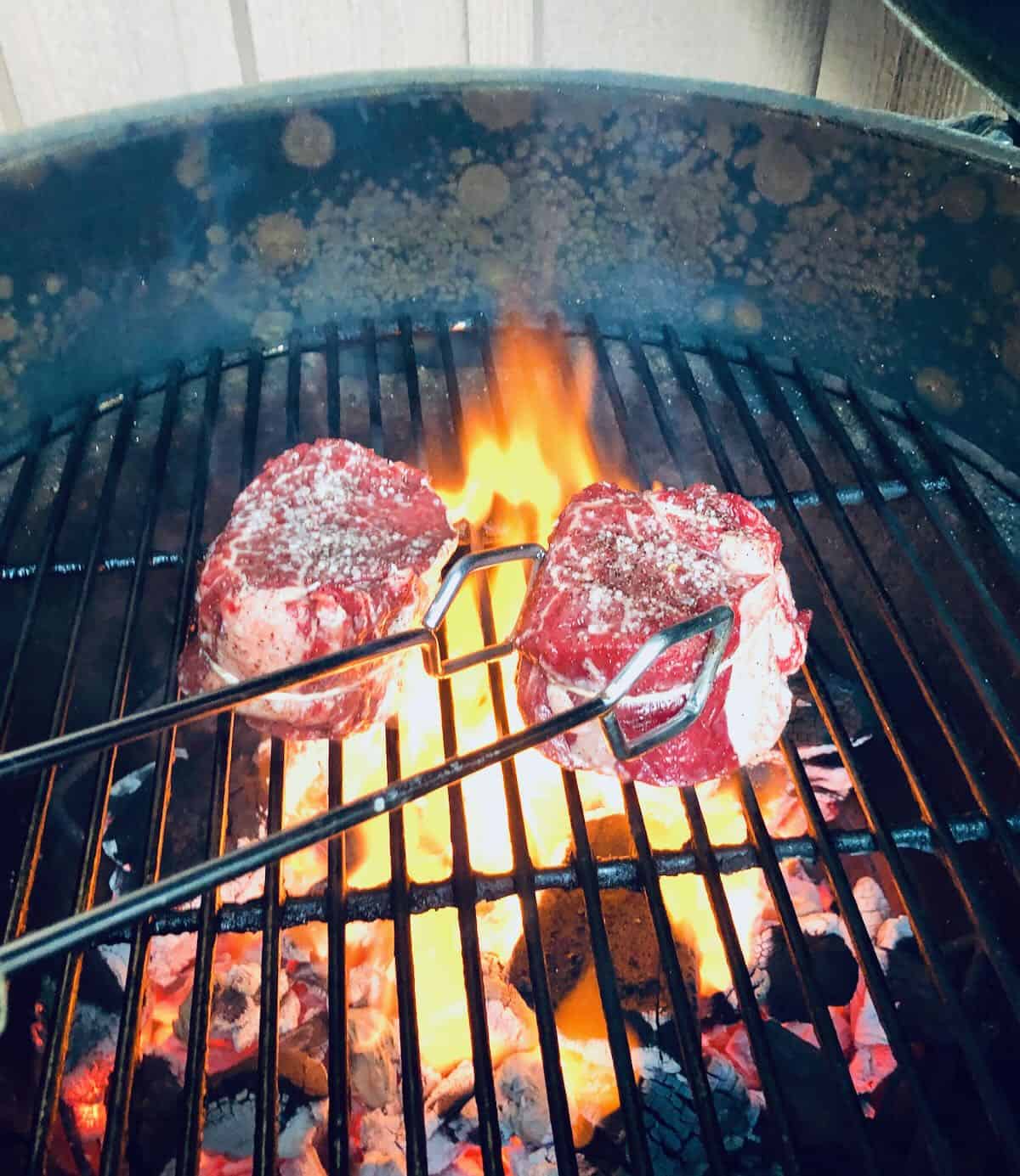Two steaks cooking in a charcoal grill over high heat. 
