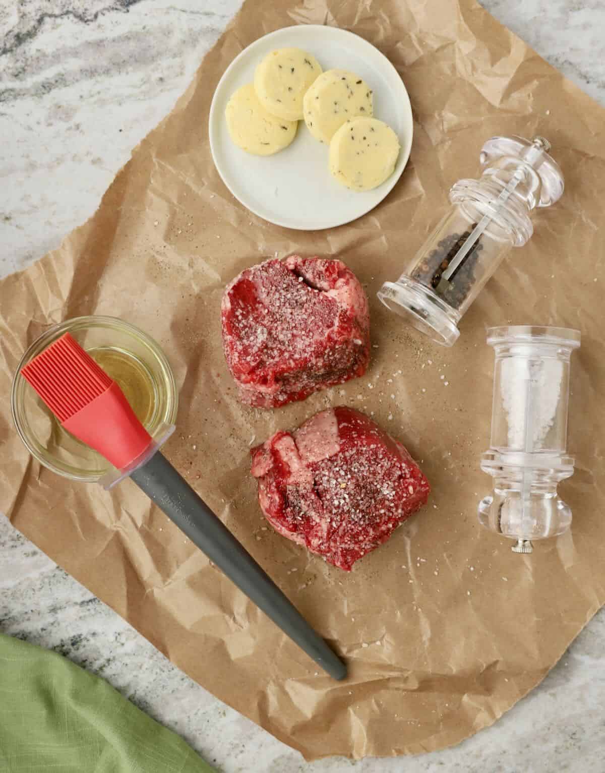 Two filet mignon steaks coated with olive oil and seasoned with salt and pepper.