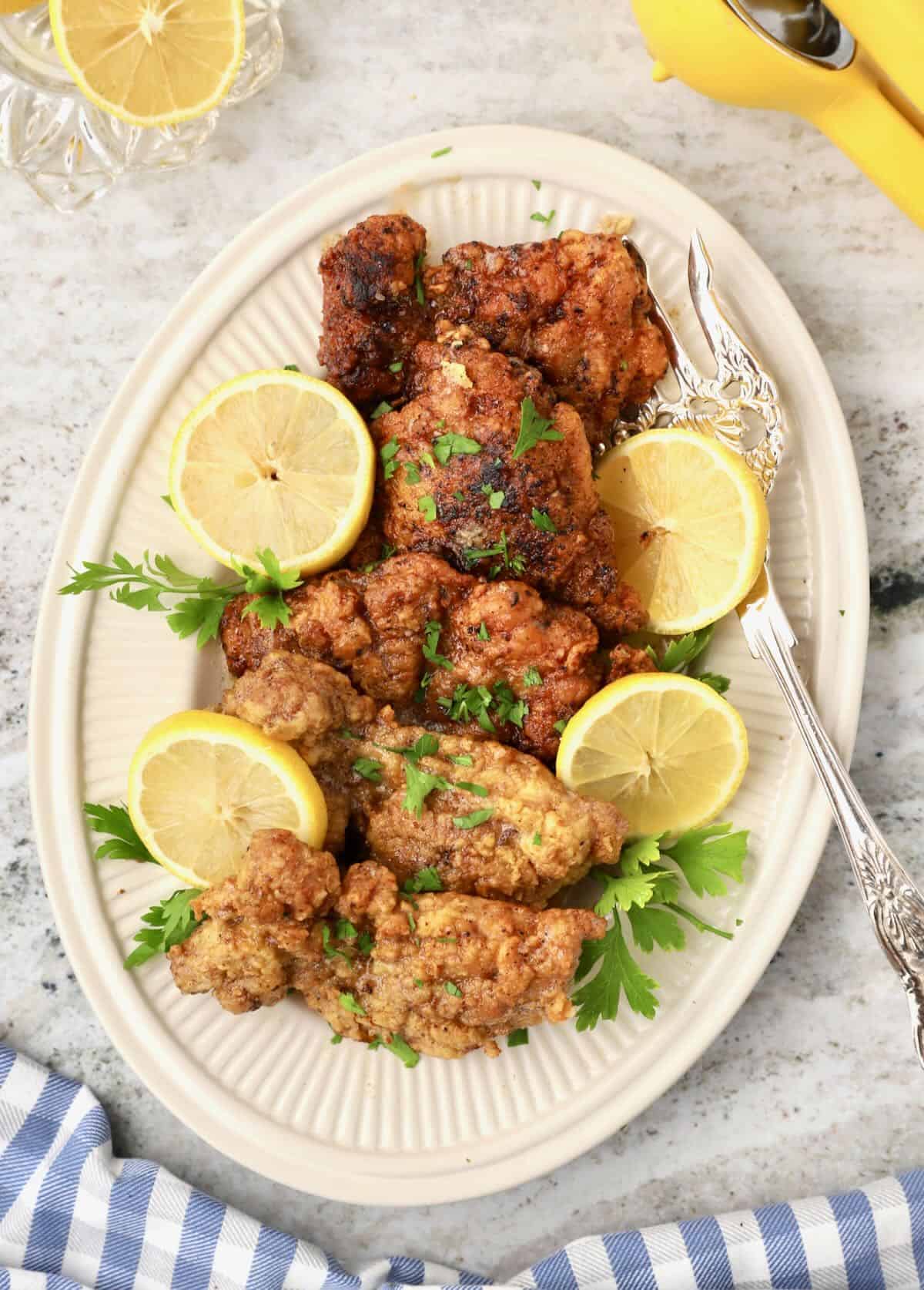 A platter full of fried chicken thighs garnished with sliced lemons.