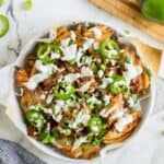 A round baking dish full of loaded fries topped with sour cream and sliced jalapenos.