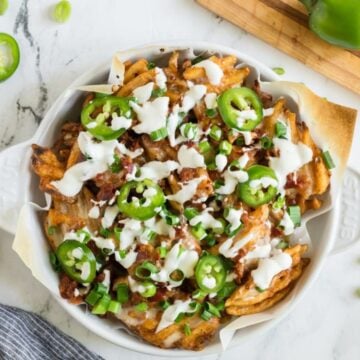 A round baking dish full of loaded fries topped with sour cream and sliced jalapenos.