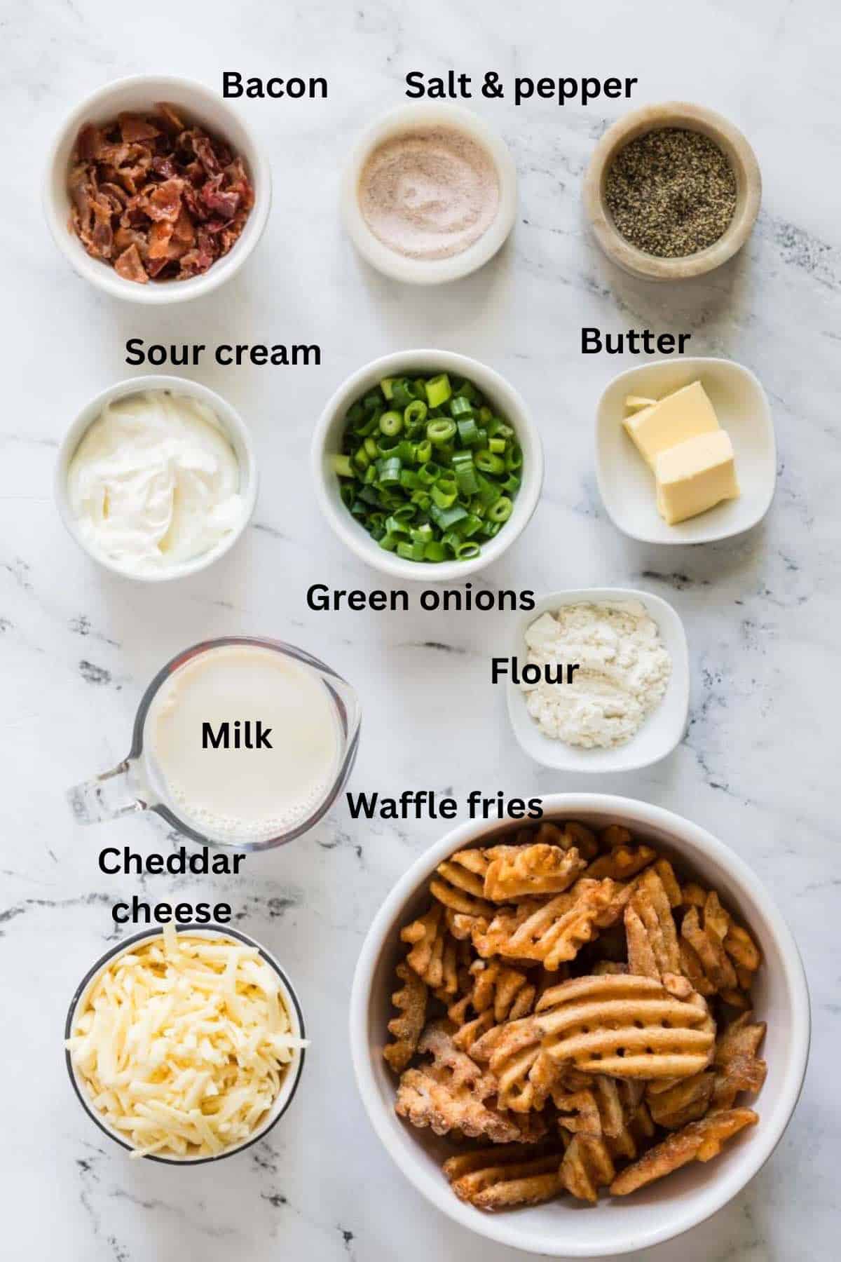 Ingredients for loaded fries include a bowl of waffle fries, sour cream, cheese, bacon, and green onions. 