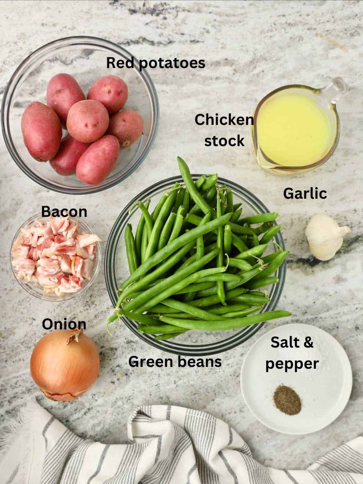 Green beans, red potatoes, bacon, chicken stock, and onions on a countertop. 