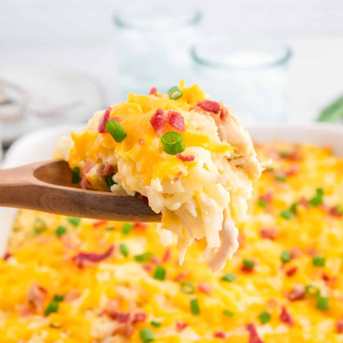 A wooden spoon holding a serving of hashbrown chicken casserole over the dish.