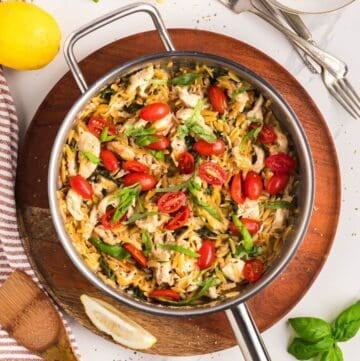 A skillet full of lemon chicken orzo pasta garnished with sliced cherry tomatoes and basil.