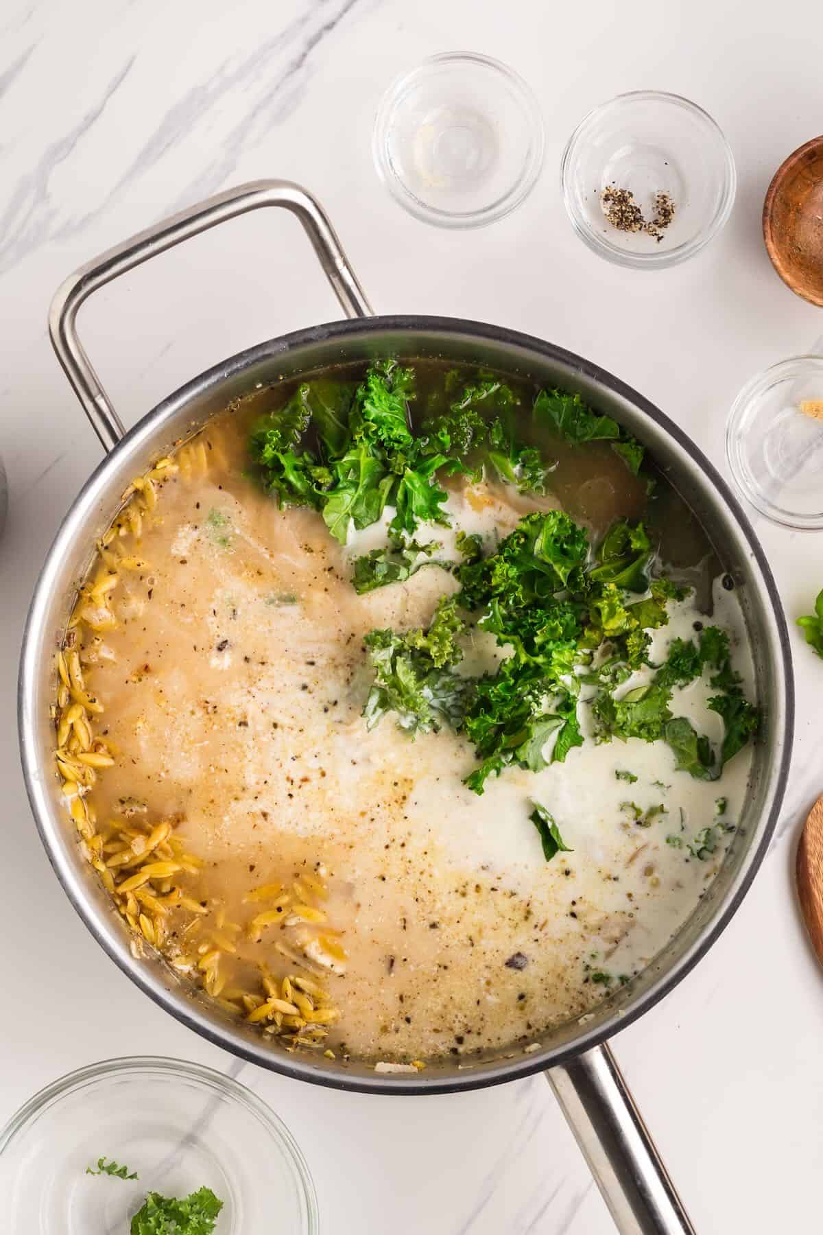 Kale, chicken stock, and heavy cream are added to a skillet with toasted orzo.