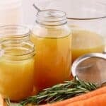 Three jars full of rotisserie chicken stock, a sprig of rosemary, and some carrots.