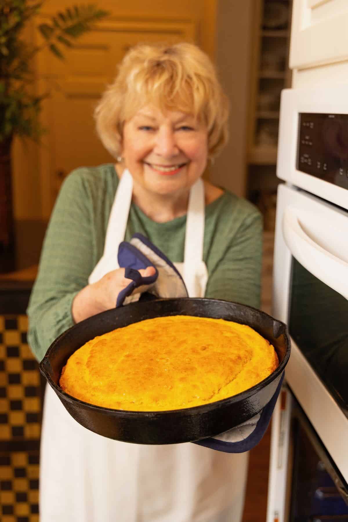 Sharon Rigsby holding a large cast iron skillet with baked cornbread. 