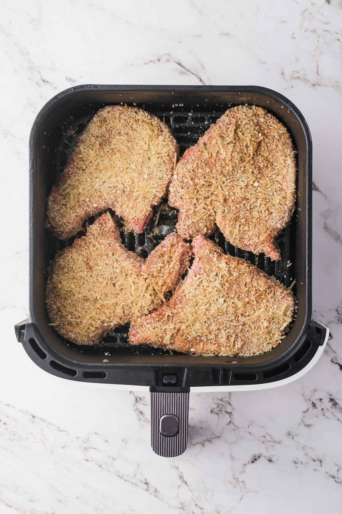 Air fryer basket with four pork chops coated with breadcrumbs. 