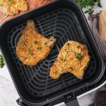 Two breaded pork chops cooked in an air fryer garnished with parsley.