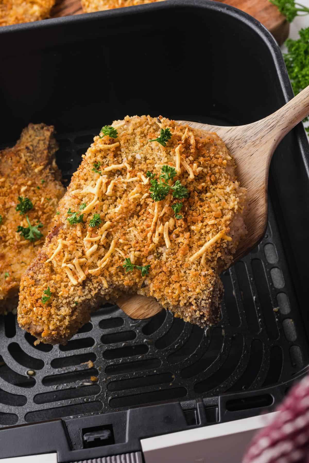 A pork chop coated in breadcrumbs and cooked in an air fryer being removed from the fryer.
