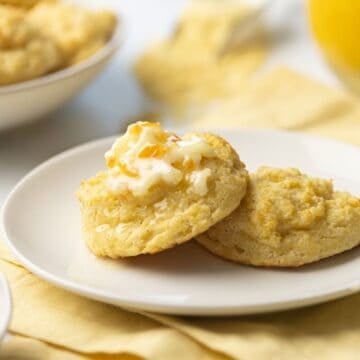 Cornmeal biscuits split on a plate, topped with a scoop of orange butter.