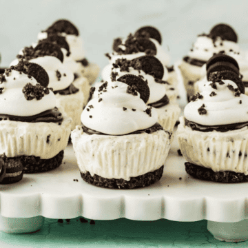 Mini Oreo cheesecakes topped with whipped cream and crushed Oreos on a serving platter.