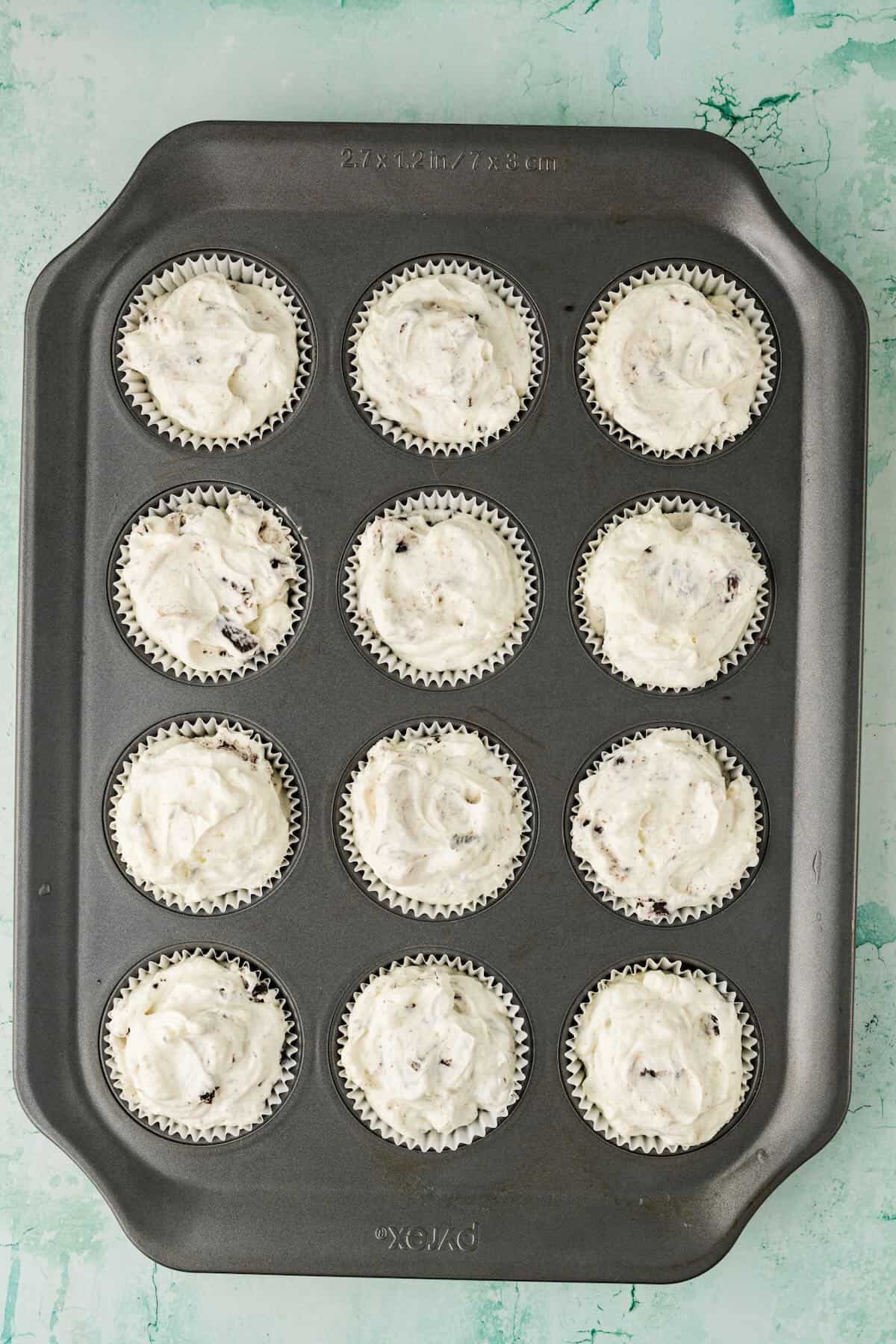 Muffin pan with cups filled with cheesecake mixture.