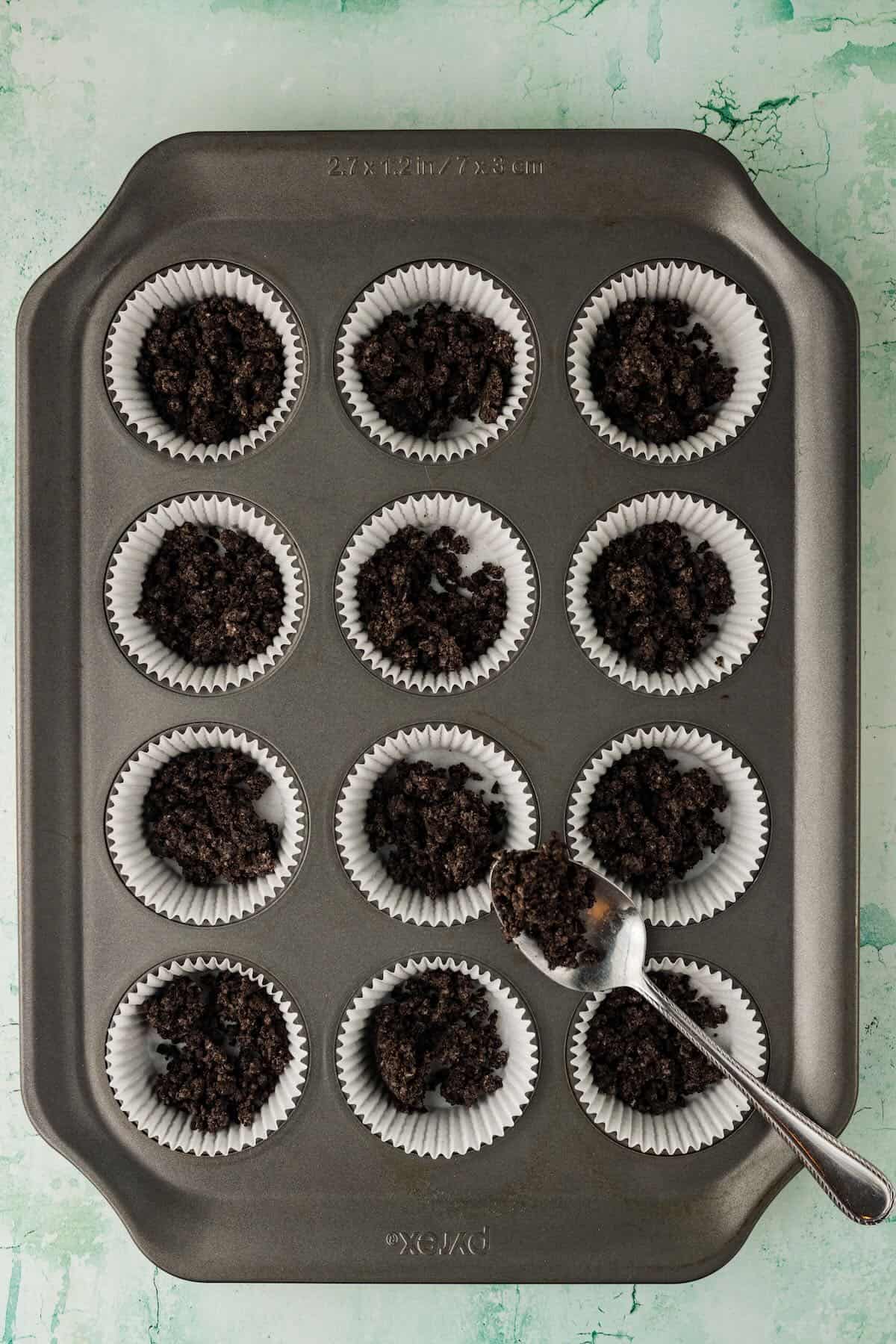 Adding crushed Oreos to muffin pan cups.