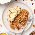 A white plate with sliced pecan crusted chicken breast and a serving of mashed potatoes.