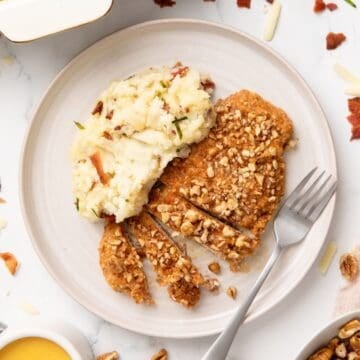 A white plate with sliced pecan crusted chicken breast and a serving of mashed potatoes.