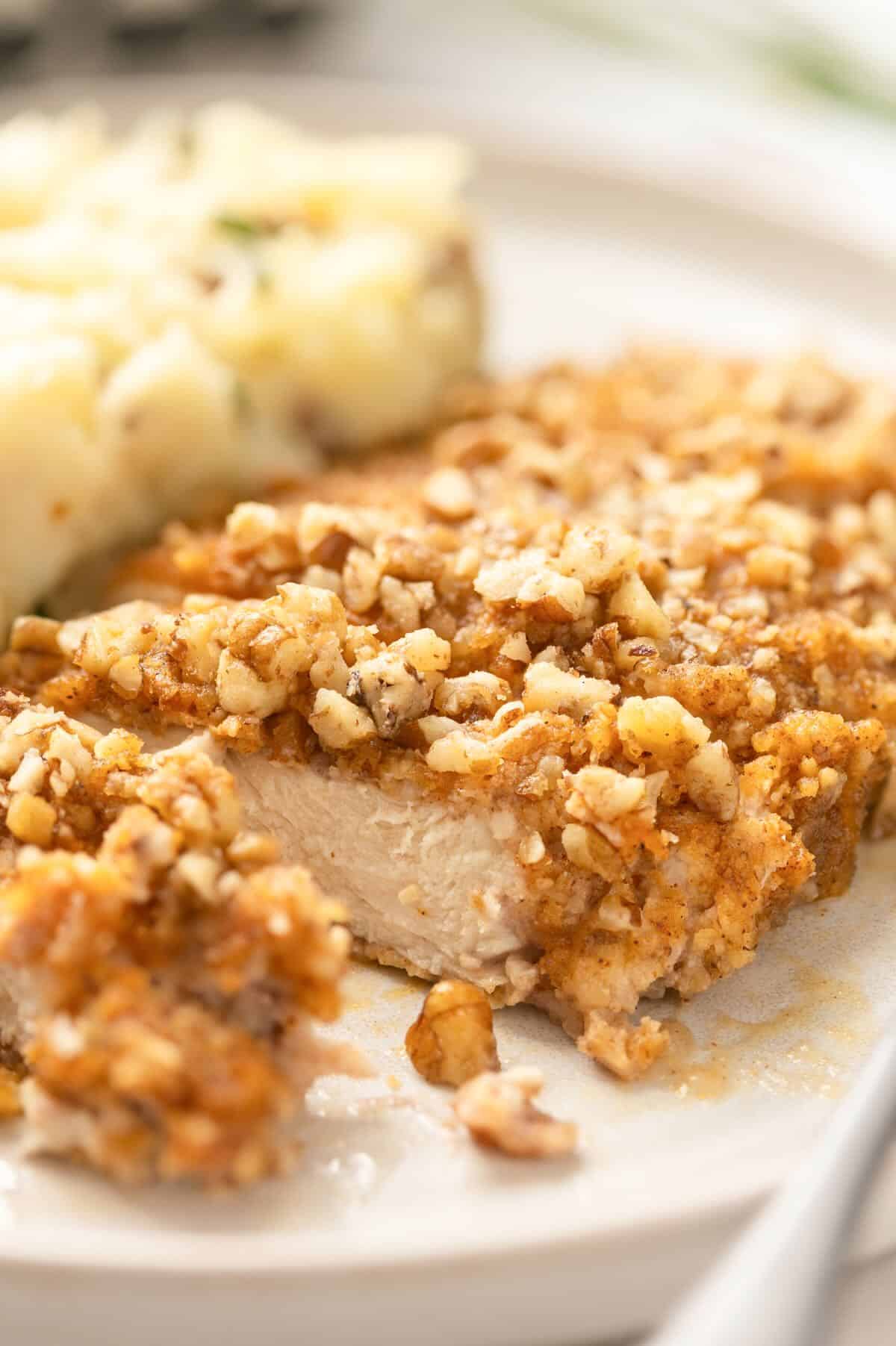 A pecan crusted chicken breast sliced on a white plate.