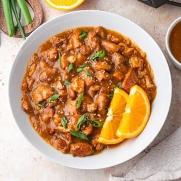 A white bowl full of Slow Cooker Orange Chicken, garnished with orange slices.