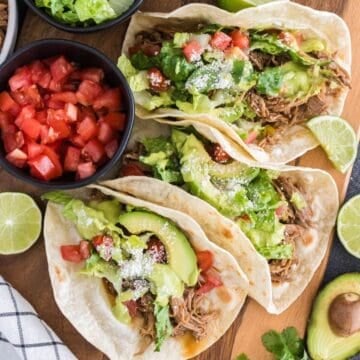 Three slow-cooker pulled pork tacos on a board with avocado cilantro lime sauce.