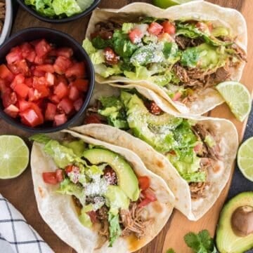 Three slow-cooker pulled pork tacos on a board with avocado cilantro lime sauce.
