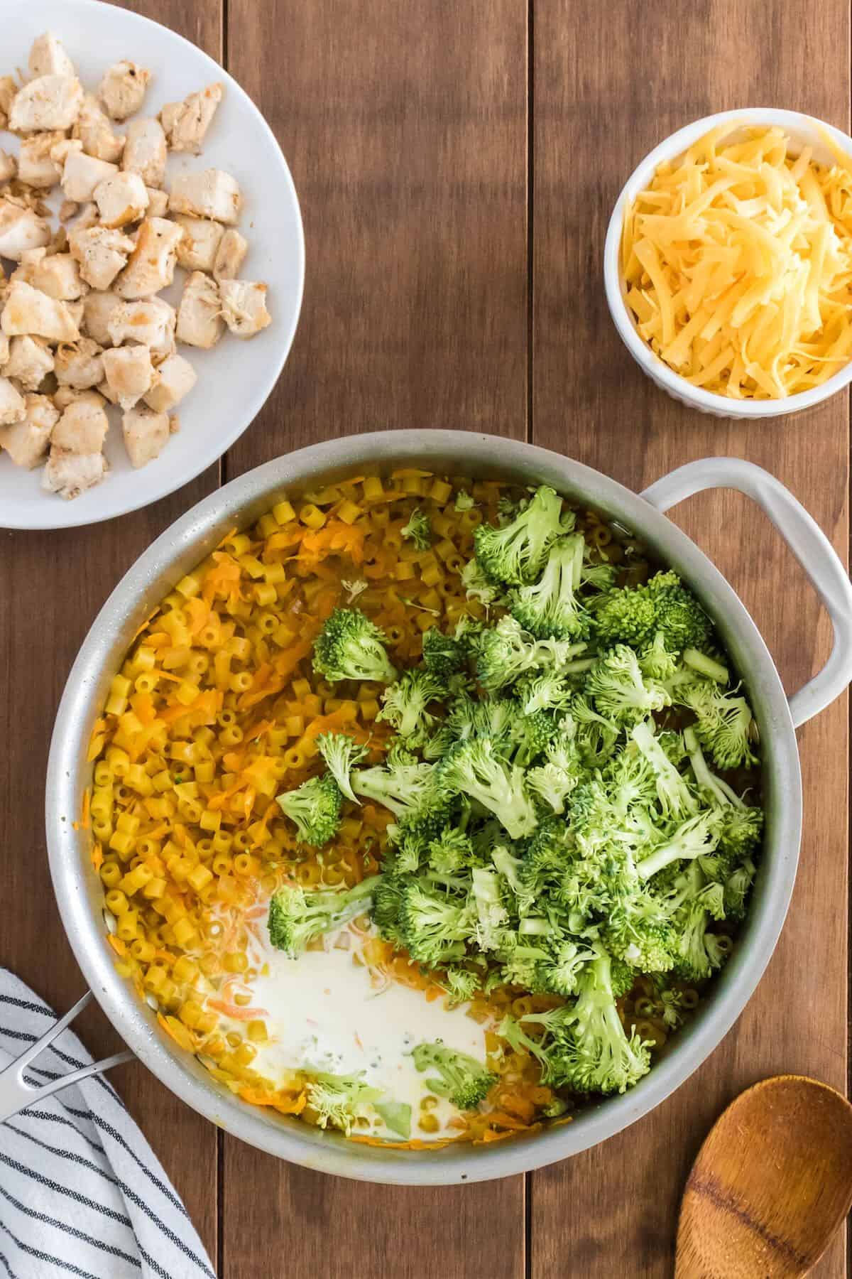 Chopped broccoli is added to a skillet along with pasta and cream.