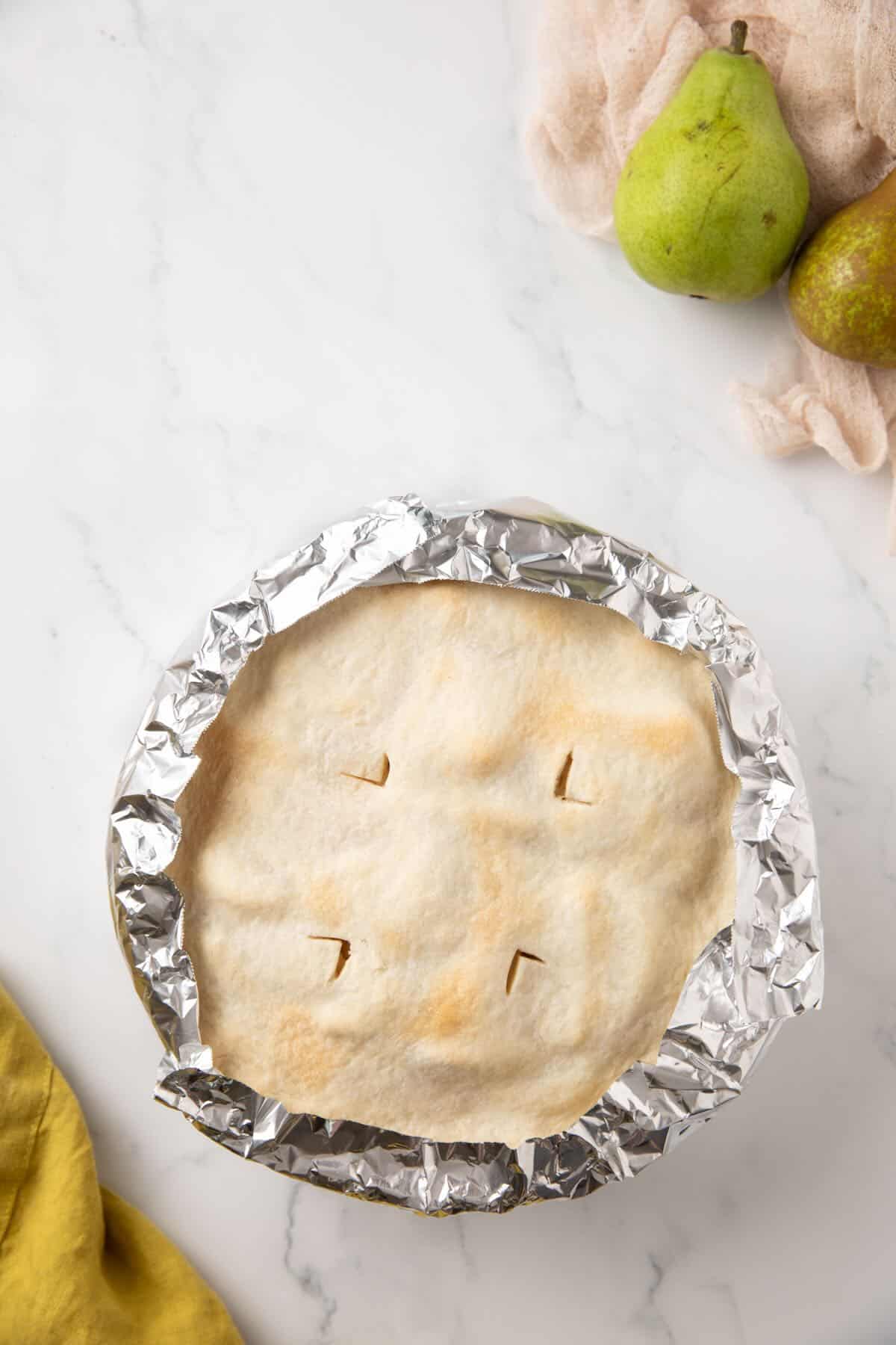 Partially baked pear pie with strips of foil wrapped around the edges to prevent over-browning. 