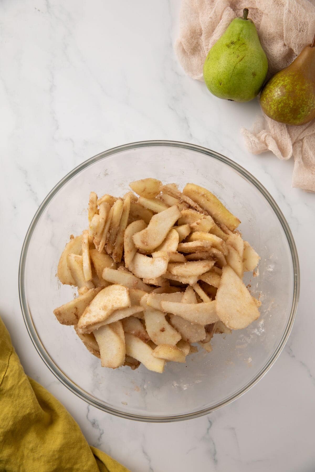 Sliced pears in a bowl mixed with cinnamon, nutmeg, and granulated and brown sugar. 