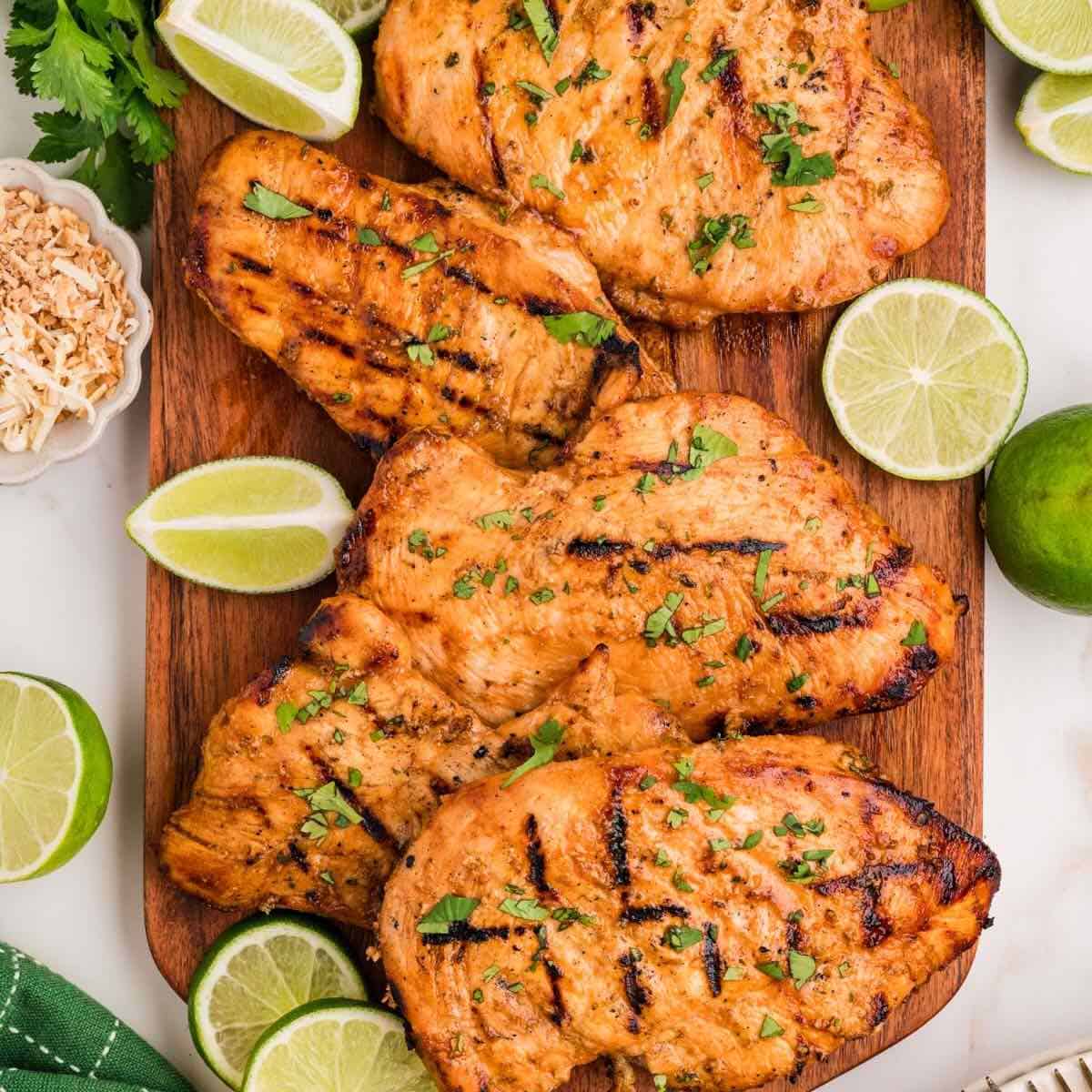 Grilled Coconut Lime Chicken breasts on a cutting board with cut limes as garnish!