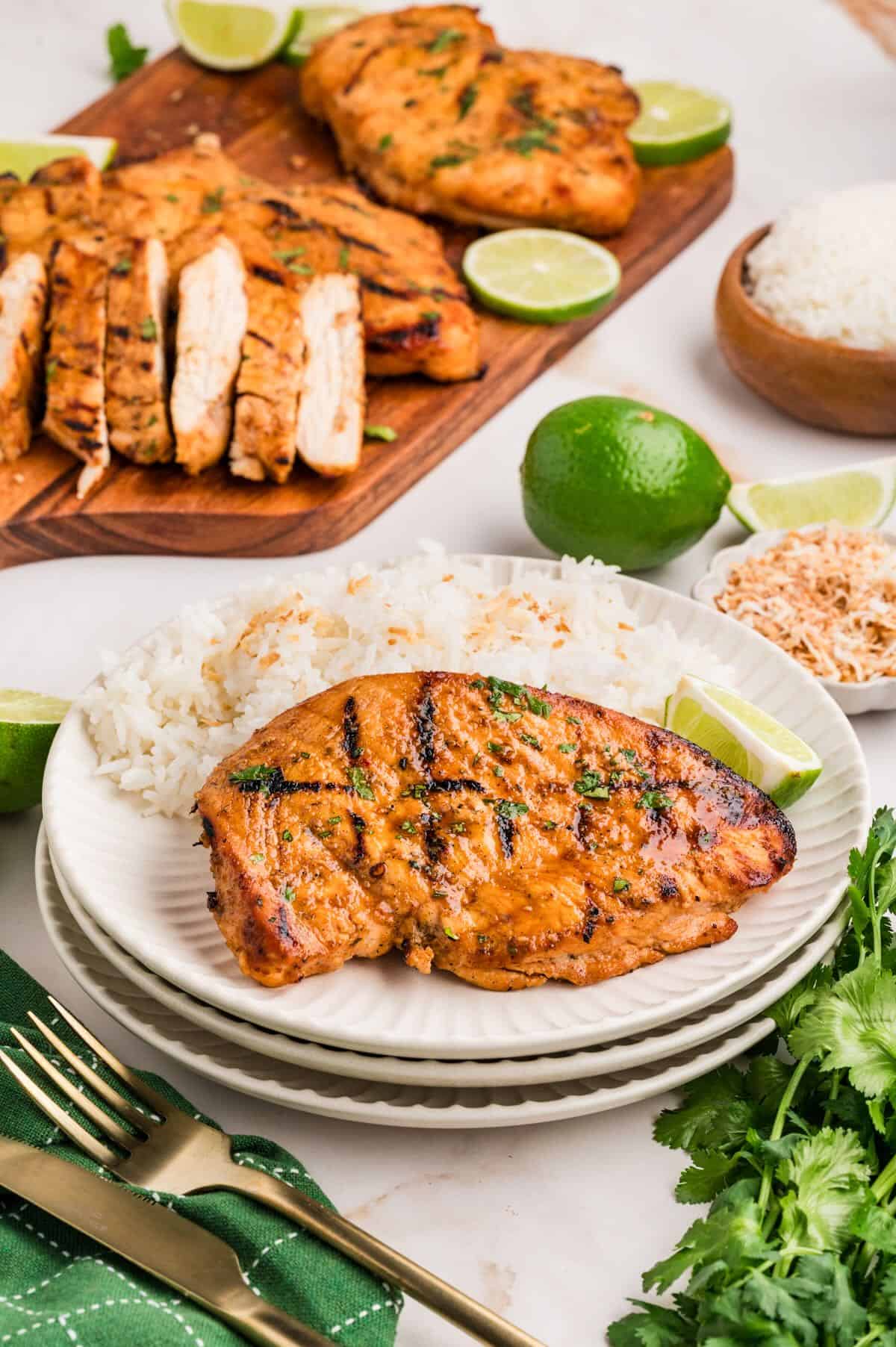 Grilled coconut lime chicken breast on a white plate with a side of coconut rice.