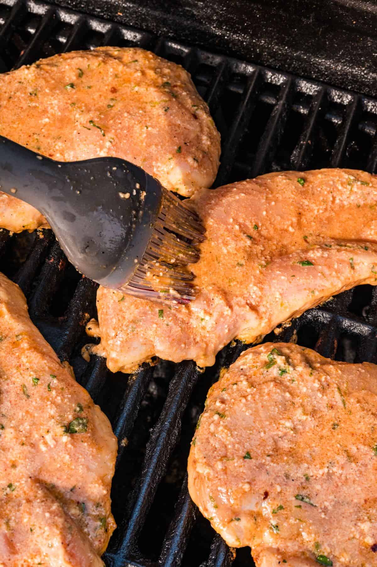 Chicken breasts on a grill with marinade being brushed over it. 