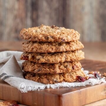 A stack of five Oatmeal Cranberry Chocolate and Pecan Cookies on a cutting board.