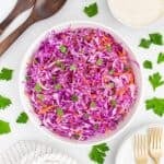 A large bowl of purple cabbage coleslaw with shredded carrots on a table.