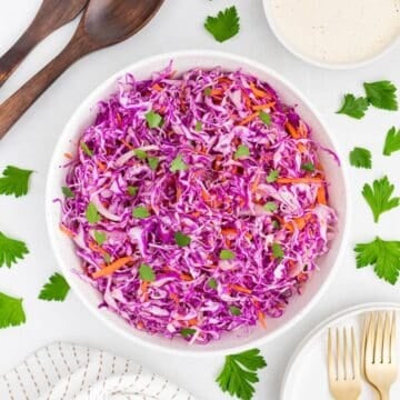 A large bowl of purple cabbage coleslaw with shredded carrots on a table.
