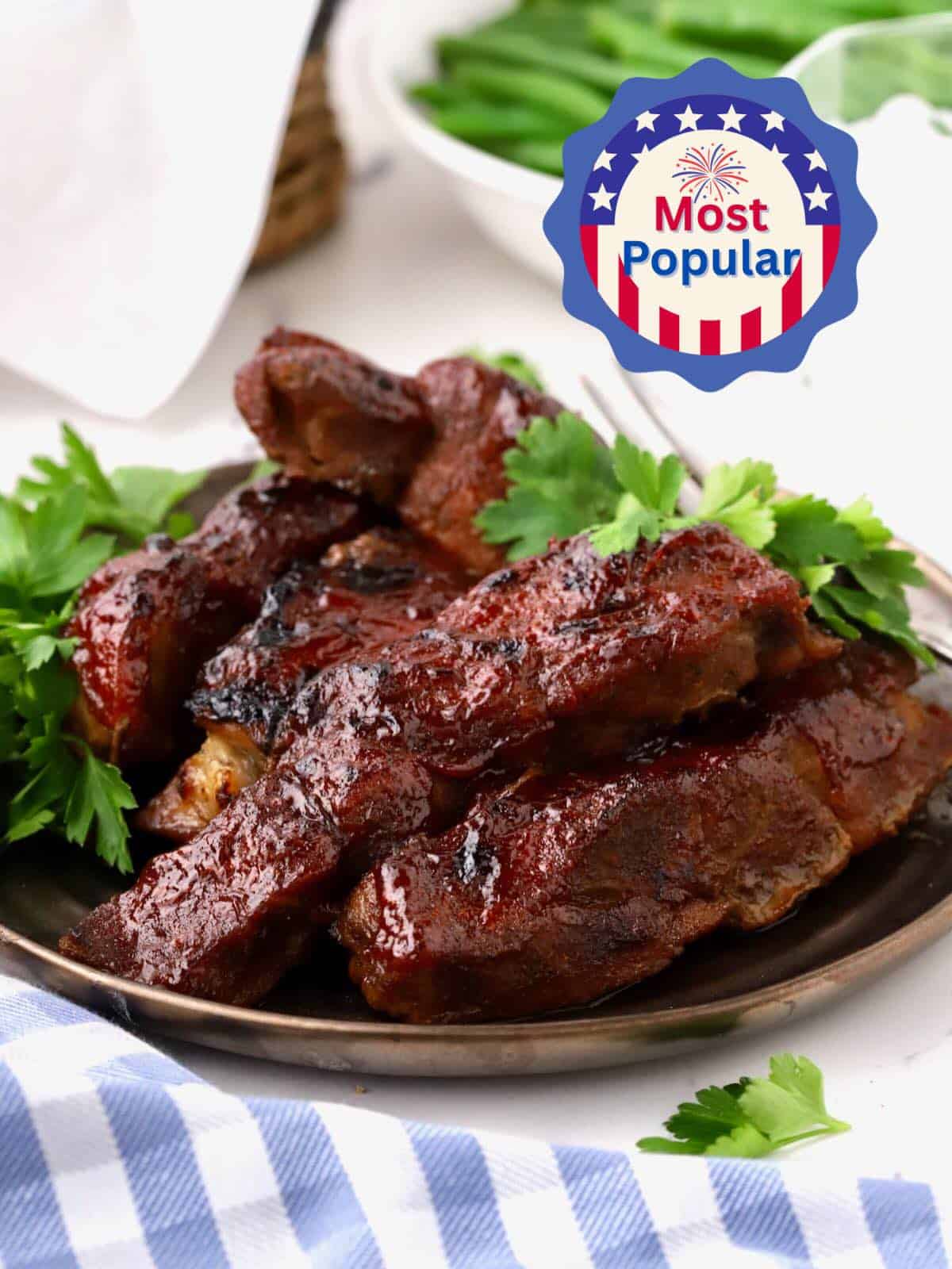 A plate of oven-baked country-style ribs topped with BBQ sauce and garnished with parsley.
