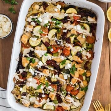 A white baking dish with baked Mediterranean Chicken and Rice Casserole topped with tahini sauce.