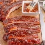 A rack of smoked spare ribs with BBQ sauce is sliced and on a cutting board.