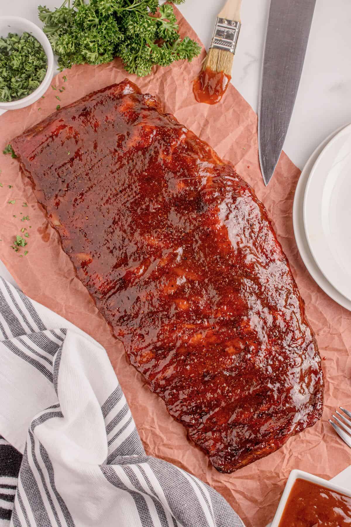 A smoked rack of ribs topped with BBQ sauce ready to slice. 