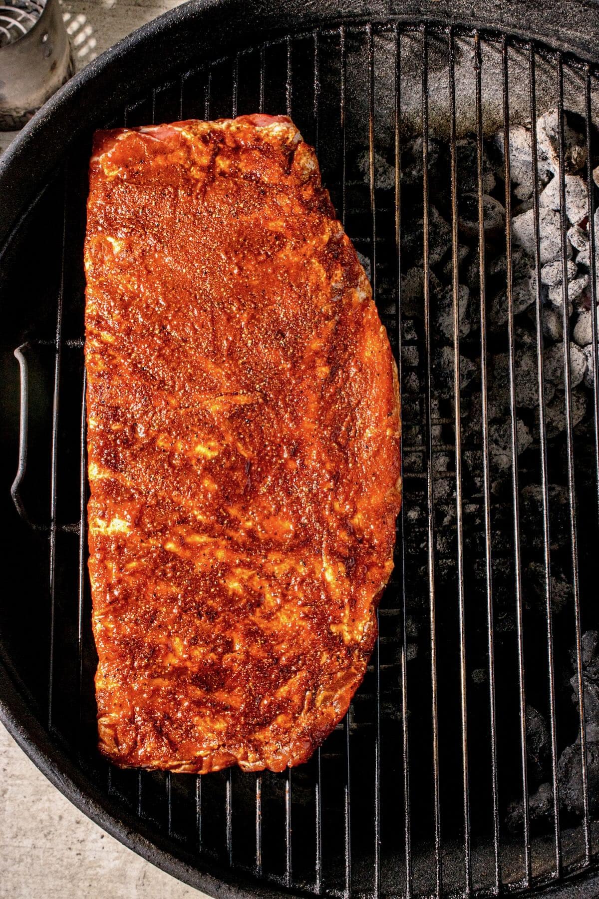 A rack of ribs topped with a dry rub cooking on a charcoal grill. 