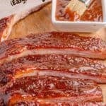 A slab of smoked ribs cut into slices on a cutting board, with text.