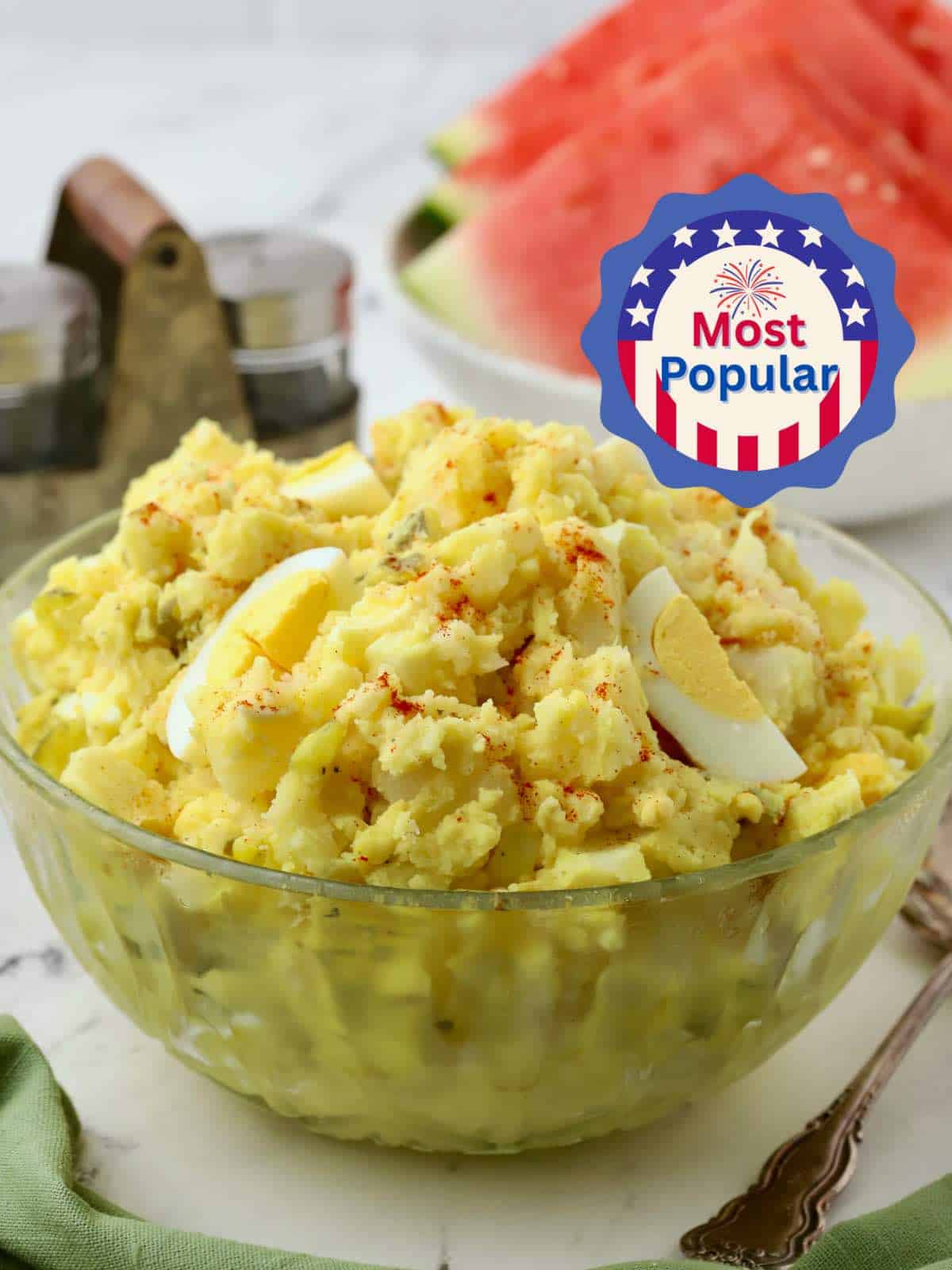 A large glass bowl of southern potato salad garnished with sliced eggs and paprika. 